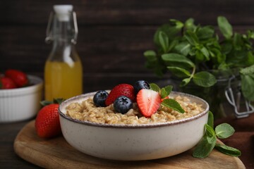 Tasty oatmeal with strawberries and blueberries in bowl on wooden table