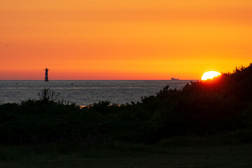 Colorful sunset over the ocean with the sun behind dunes of the baltic sea and a lighthouse