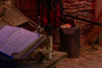 A severed hand by the executioner's ax on a log in the torture chamber.