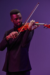 Elegant man in black suit playing violin on vibrant purple background, creating a harmonious and...
