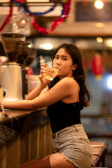 A young woman is sipping a cold alcoholic drink. While sitting at the bar in a rustic cafe and looking at camera.