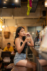 A young woman is sipping a cold alcoholic drink. While sitting at the bar in a rustic cafe and looking at camera.