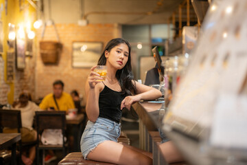 A young woman is sipping a cold alcoholic drink. While sitting at the bar in a rustic cafe and looking at camera.