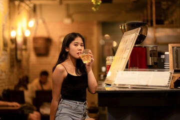 A young woman is sipping a cold alcoholic drink. While sitting at the bar in a rustic cafe and looking at camera.