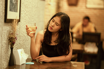 A woman drinks alone at a wooden table in a warmly lit cafe.