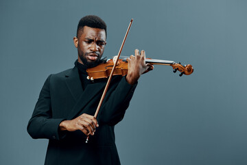 Elegant black violinist in a formal suit performing on violin against a neutral gray backdrop