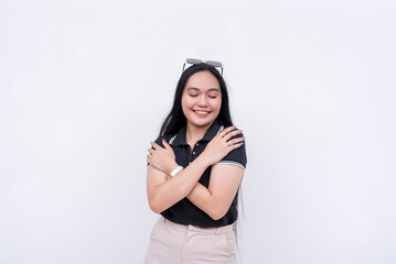 Young Asian woman smiling and embracing herself on a white background