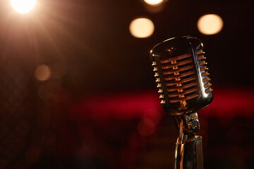 Closeup background image of metal retro microphone on stage with blurred audience seating copy space
