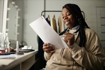 Portrait of smiling African American woman rehearsing lines in dressing room while getting ready...