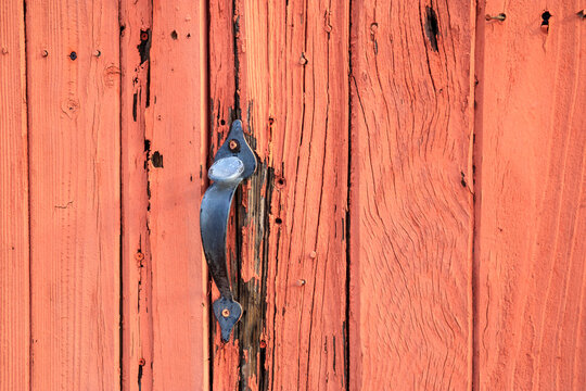 Vintage S-grip metal handle and thumb paddle screw mounted on a rundown heavily weathered red wooden door