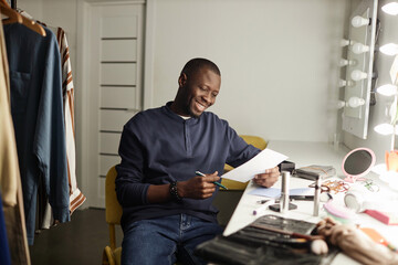 Portrait of smiling Black man reading script while preparing for performance backstage