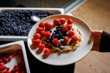 pancakes adorned with ripe red strawberries and juicy blueberries, complemented by a luscious cream topping.