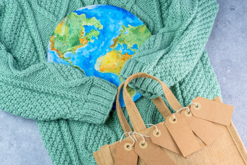 The sweater sleeves holding the tags in the embrace of the planet with an eco bag. Responsible...
