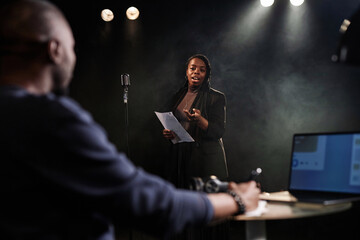Portrait of Black young woman performing on stage with theater director watching rehearsal or...