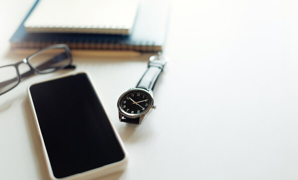 Close-up shot, wrist watch with mobile phone, notebook, eyeglasses on white table