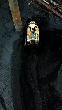 Bulldozer sorts coal. Extractive industry, anthracite. Coal industry. Aerial view. Vertical video