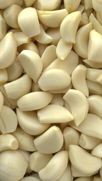 Top view of a lot of peeled garlic cloves as an abstract food pattern;  Table spin. Vertical video;