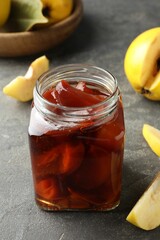 Tasty homemade quince jam in jar and fruits on grey textured table