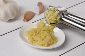 One metal press and garlic on white wooden table, closeup