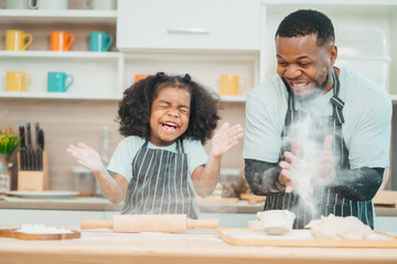 In a home kitchen, black father and his daughter bond over cooking a meal food, their laughter and...