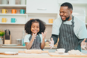 In a home kitchen, black father and his daughter bond over cooking a meal food, their laughter and...
