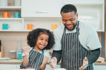In a home kitchen, black father and his daughter bond over cooking a meal food, their laughter and love filling the air, embodying the joy of African American family life, Father's Day concept - 765031774