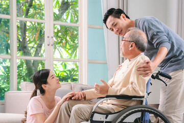 Celebrating Father's Day, Senior Asian grandfather in a wheelchair shares a happy moment at home, hugging his family together, symbolizing generational love and care, health care and life insurance - 765031926