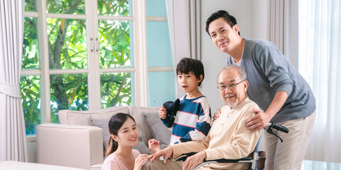 Celebrating Father's Day, Senior Asian grandfather in a wheelchair shares a happy moment at home, hugging his family together, symbolizing generational love and care, health care and life insurance - 765031947