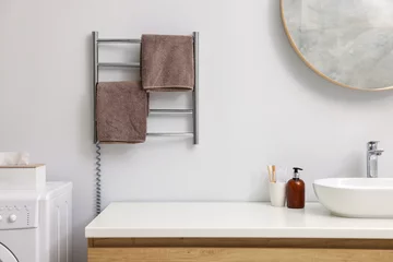 Tuinposter Heated towel rail with brown towels in bathroom © New Africa