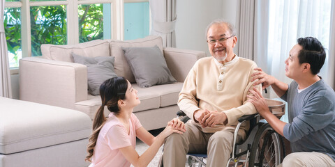 Celebrating Father's Day, Senior Asian grandfather in a wheelchair shares a happy moment at home, hugging his family together, symbolizing generational love and care, health care and life insurance - obrazy, fototapety, plakaty