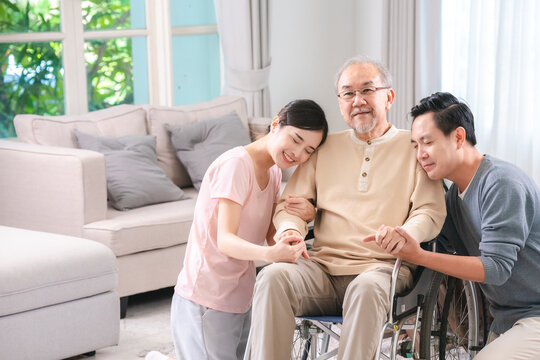 Celebrating Father's Day, Senior Asian grandfather in a wheelchair shares a happy moment at home, hugging his family together, symbolizing generational love and care, health care and life insurance