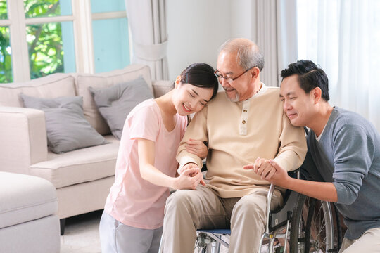 Celebrating Father's Day, Senior Asian grandfather in a wheelchair shares a happy moment at home, hugging his family together, symbolizing generational love and care, health care and life insurance