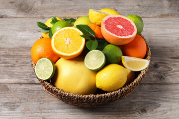 Different fresh citrus fruits and leaves in wicker basket on wooden table, closeup