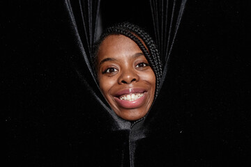 Close up of smiling African American woman peeking from curtains on theater stage and looking at...