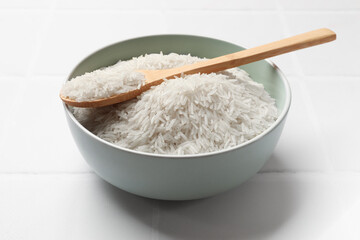 Fototapeta na wymiar Raw basmati rice in bowl and spoon on white tiled table