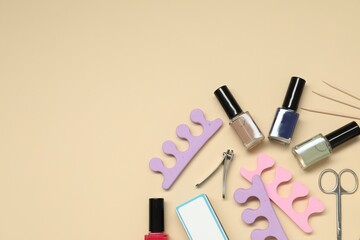 Nail polishes and set of pedicure tools on beige background, flat lay. Space for text