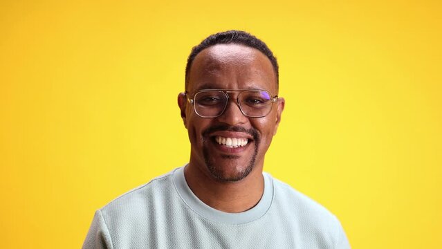 Happy and excited African-American man smiling and spreading hands against yellow studio background. Positive surprise. Concept of human emotions, casual fashion, lifestyle, sales, news