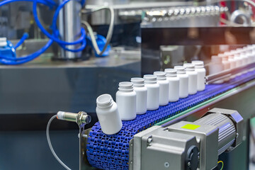Moving polypropylene white bottles on conveyor belt of automatic liquid filling machine