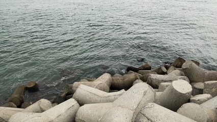 Sea water splashing after waves hitting on tetrapod a massive triangle shape concrete stone structure near beach or sea shore used to protect land from heavy ocean tidal waves. Closeup aerial view.