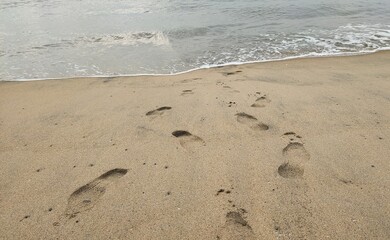 Romantic couple footprints or footsteps imprint trace marks closeup on tropical beach sand with sea water wave foam background. Peaceful seaside island journey, leisure, holiday and vacation concept.