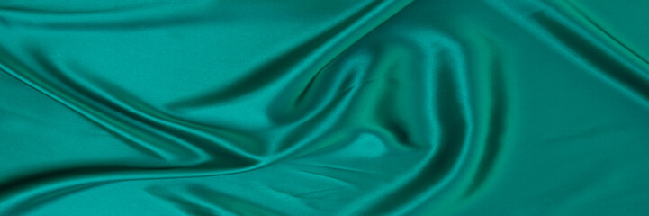 Black green satin dark fabric texture luxurious shiny that is abstract silk cloth background with...