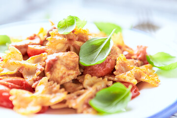 Farfalle pasta with chicken breast, cherry tomatoes and fresh basil. Bright wooden background. Close up.	