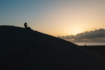 Silhouette of a woman watching the sunrise from the top of a dune.