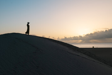 Fototapeta na wymiar Silhouette of a woman with her hat on a dune watching the sunrise