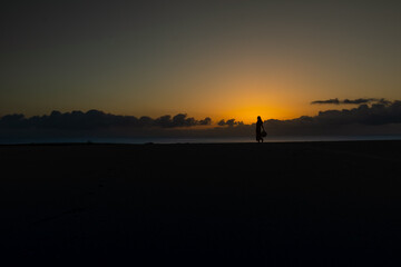 Silhouette of woman holding her hat in her hand in front of the rising sun