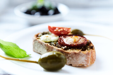 Crostini with tomato, salami and olive pesto on wooden background.