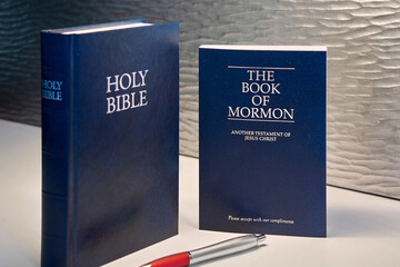 This image shows a Bible and a Book of Mormon, both in dark tones, accompanied by a red and silver...