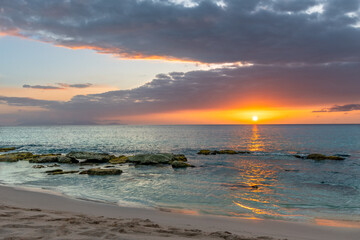 Sunset on the beach with sun setting on the horizon with large mossy rocks on the Caribbean island...