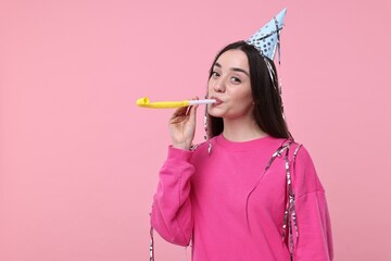 Woman in party hat with blower and streamers on pink background, space for text
