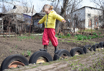 A girl walks on tires in the backyard.